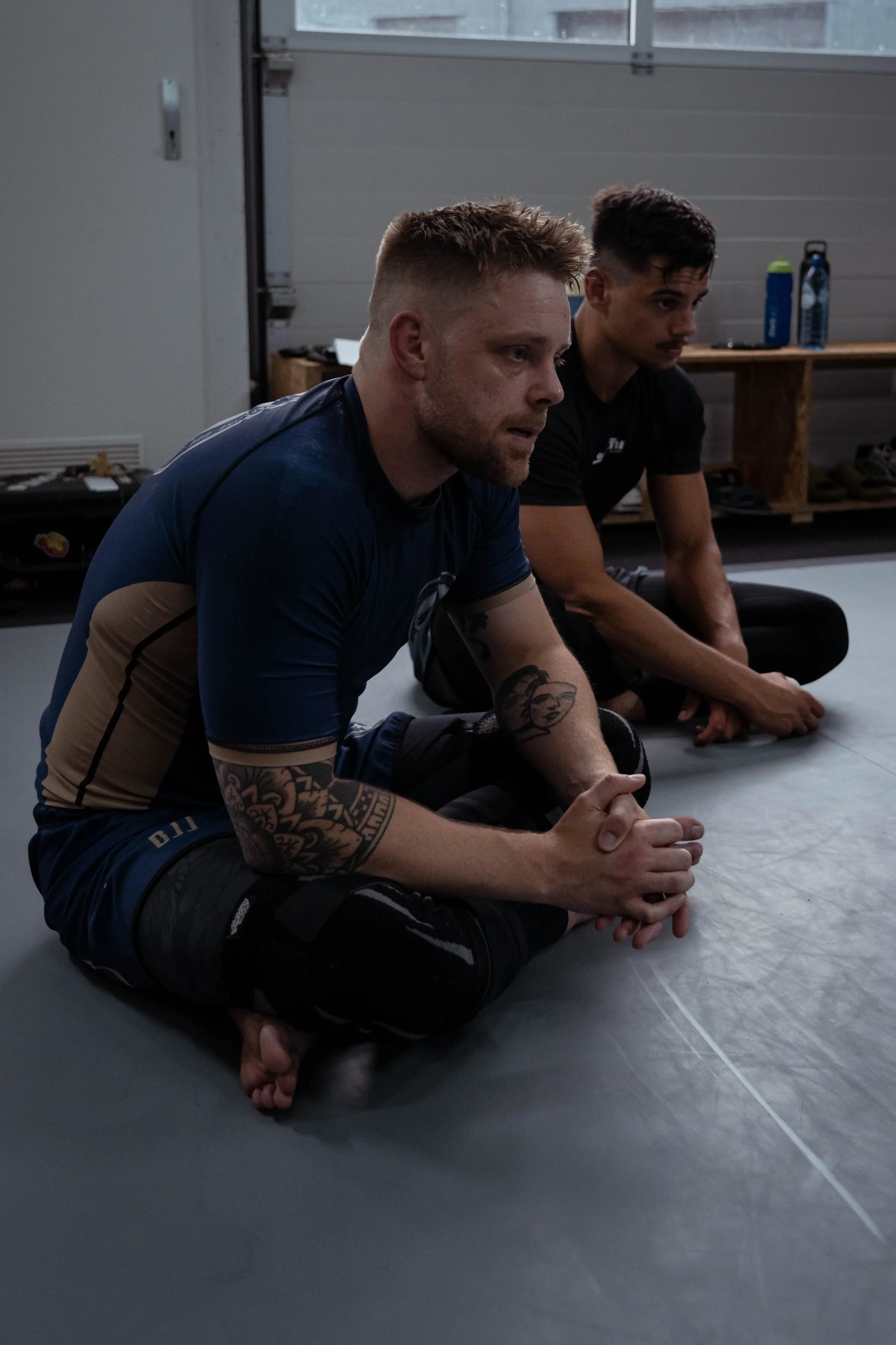 Trainer legt geknield een detail uit aan een sporter langs de mat