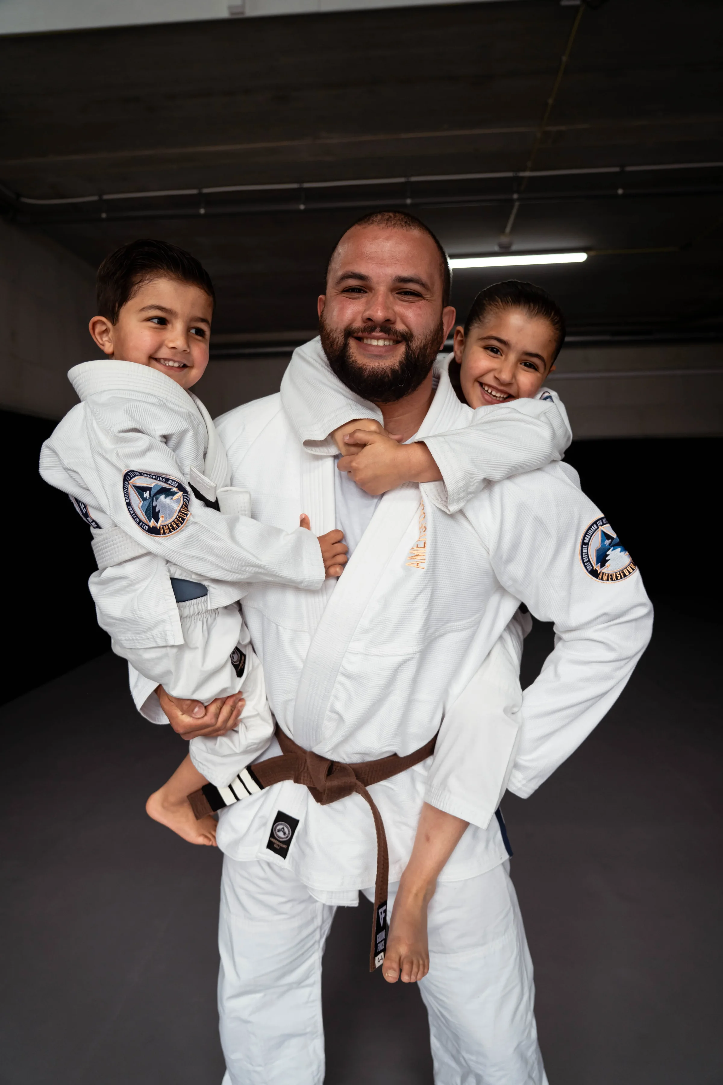 Trainer met twee lachende kinderen in gi na de BJJ-les