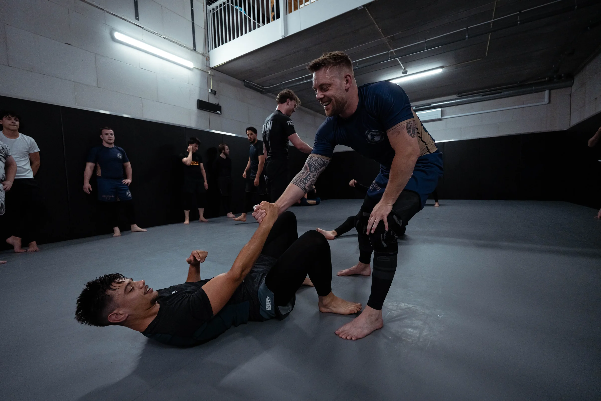 Trainer begeleidt twee volwassenen tijdens een grappling-oefening op de mat